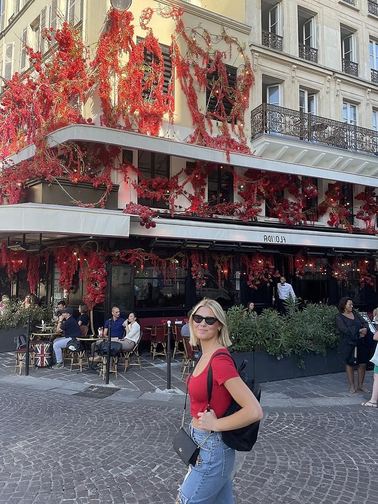 穿着红色t恤和牛仔裤的金发学生在巴黎商店前贴着相配的红色花朵.