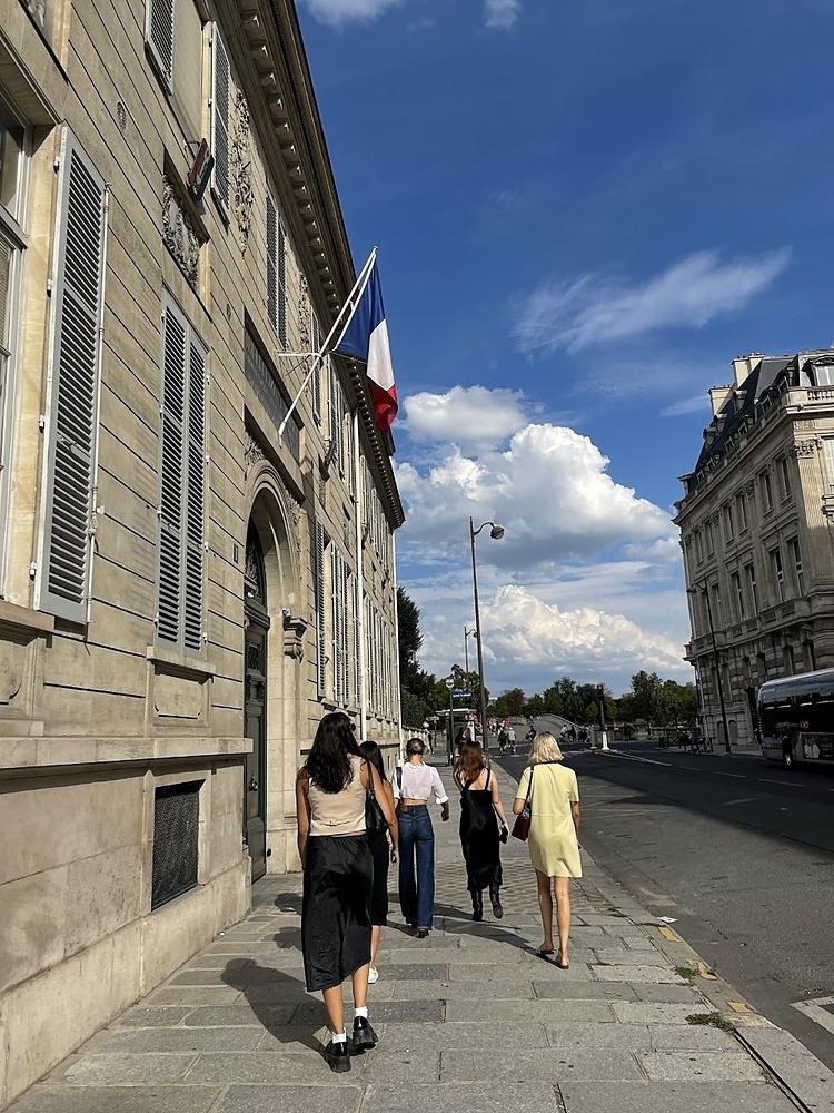 一群4个学生朋友走在巴黎的街道上，旁边是一栋米色的建筑